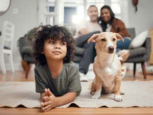 Young child playing on the floor next to small tan dog